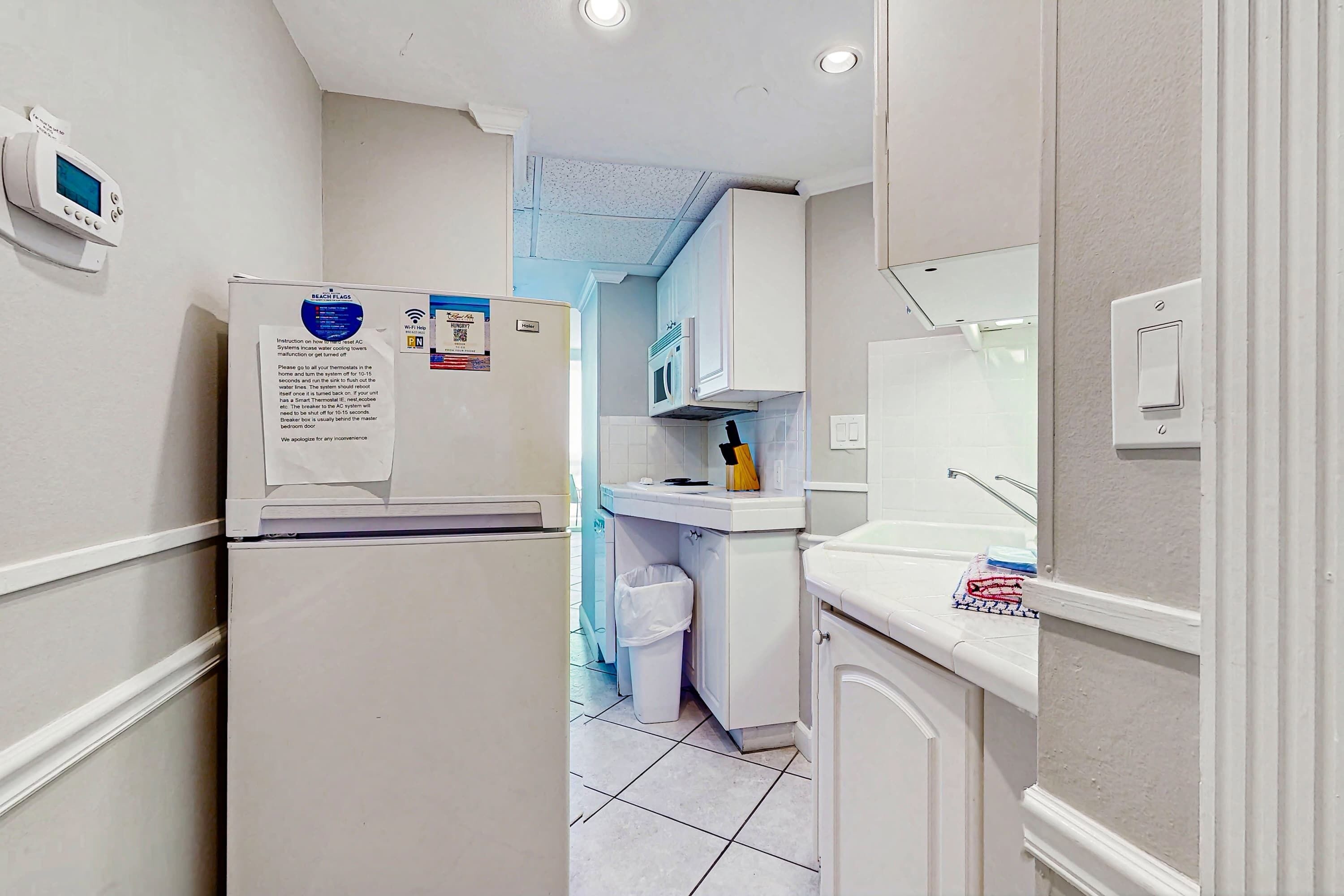 A compact kitchen with white cabinets, a refrigerator, a microwave, and a sink.