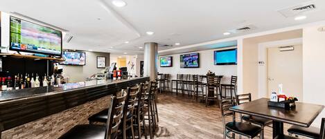 A restaurant with a bar area, multiple tables and chairs, and televisions displaying sports events.