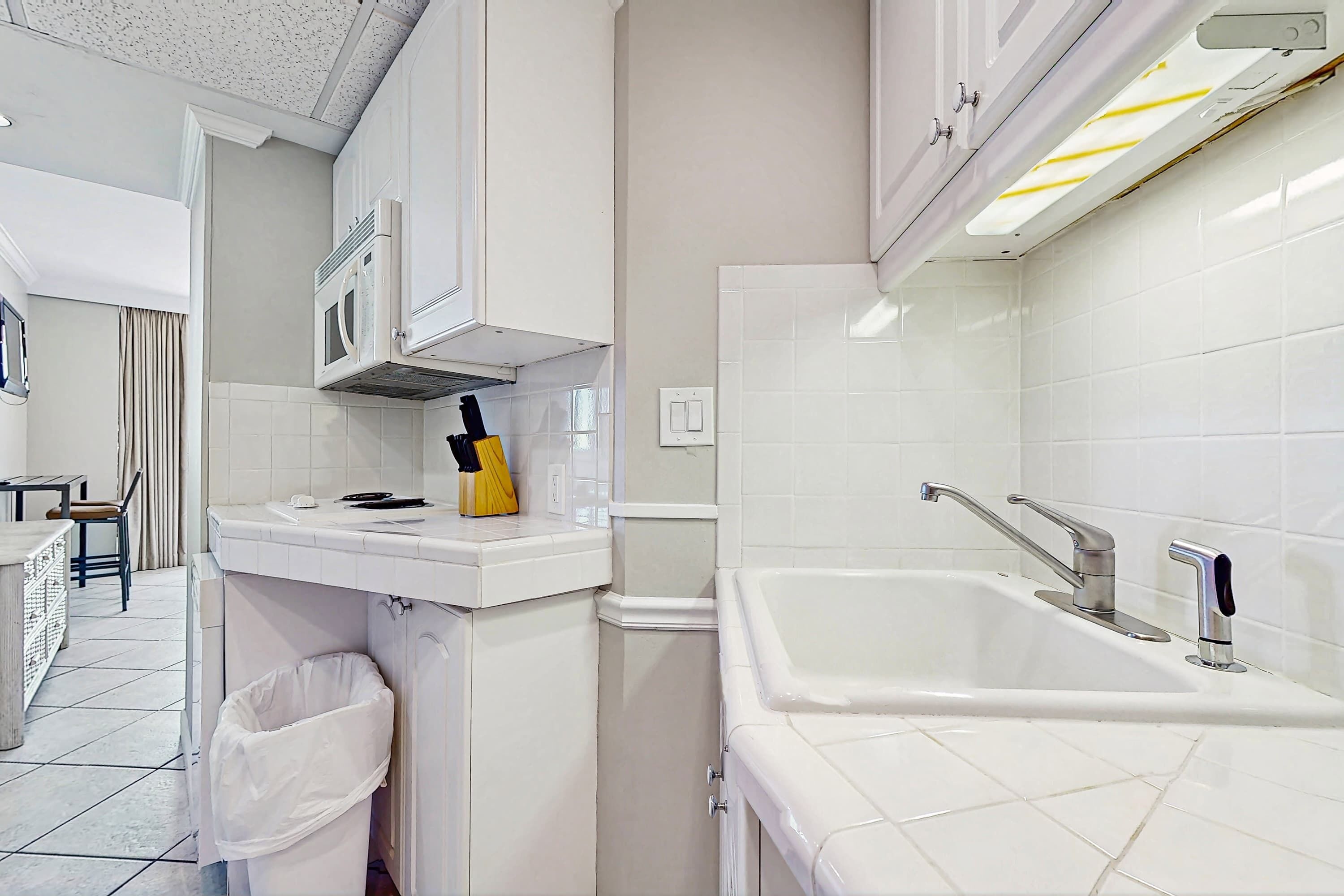A modern kitchen with white cabinets, a built-in microwave, a sink with a modern faucet, and a trash bin.