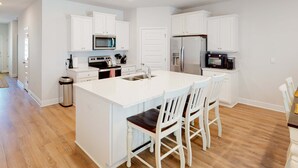A modern kitchen with white cabinetry, a central island with seating, stainless steel appliances, and a wooden floor.