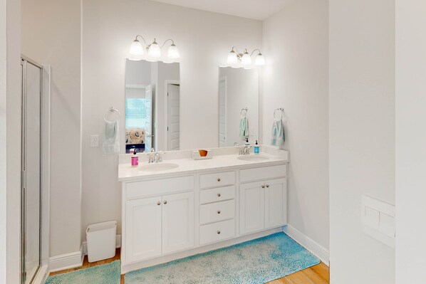 A bathroom with a white vanity, two sinks, a large mirror, and a blue rug.