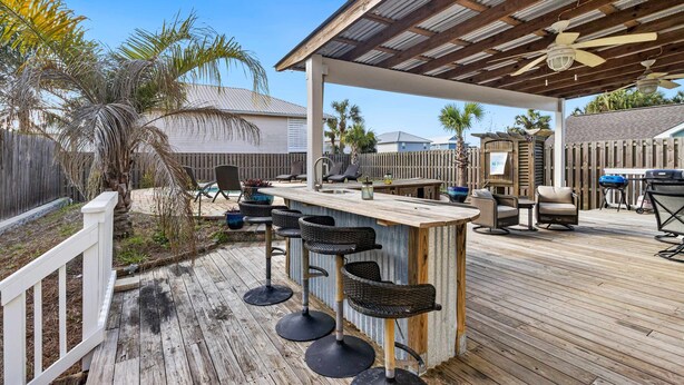 A covered outdoor patio with a wooden deck, a bar area with stools, and a ceiling fan. - Dog-friendly coastal getaway with private pool, patio, & grill (Port St. Joe)