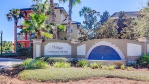 Señal de 'Villages Crystal Beach', con un arco de azulejos y un jardín ajardinado.