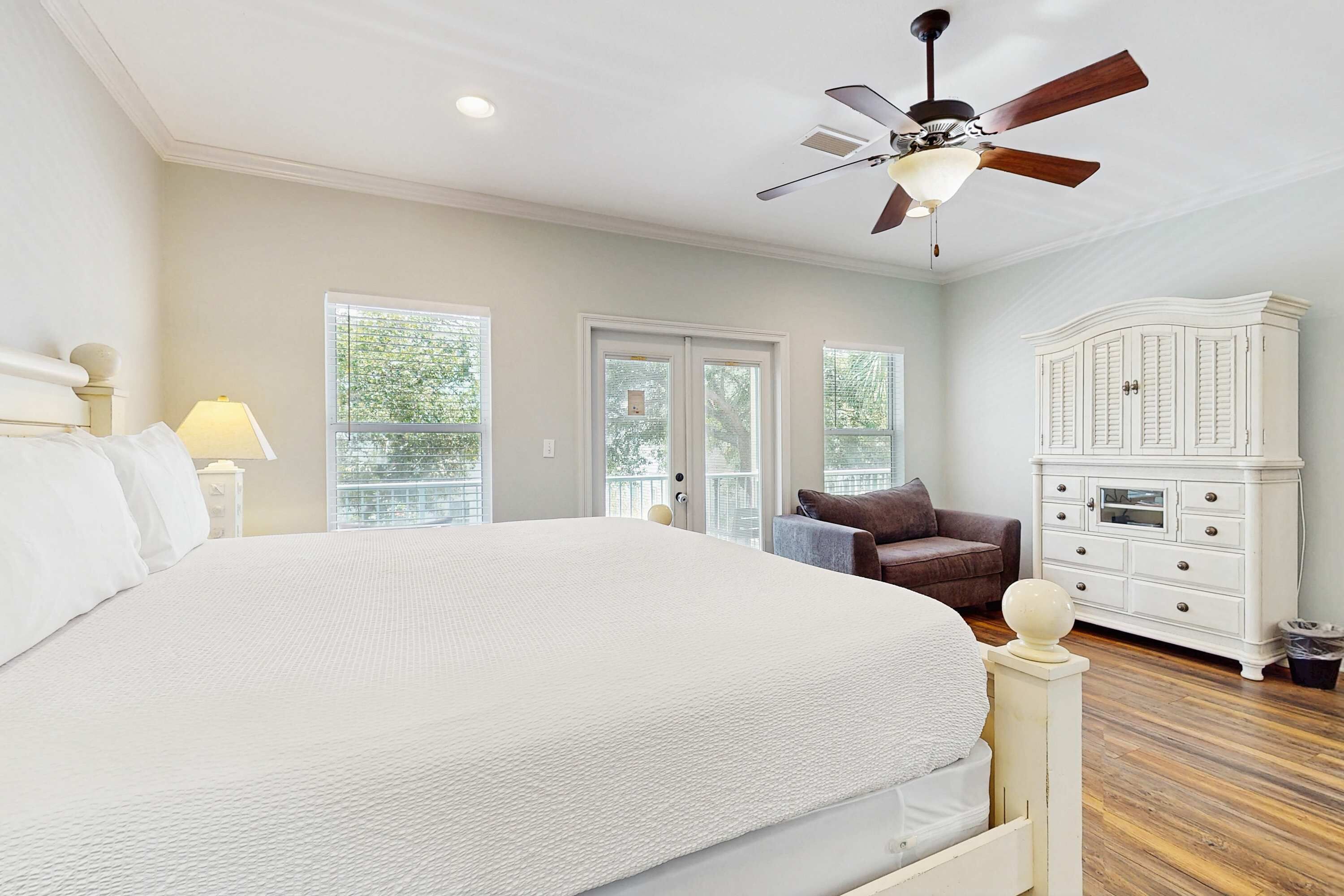 A bedroom with a large bed, a ceiling fan, a white dresser, and a brown armchair.