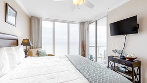 Camera d'albergo con un grande letto, una ventola a soffitto, una TV e vista sul cielo attraverso ampie finestre.