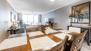 Un'area pranzo con tavolo in legno apparecchiato per quattro persone, circondato da sedie, un elemento decorativo al centro e vista sul soggiorno sullo sfondo.