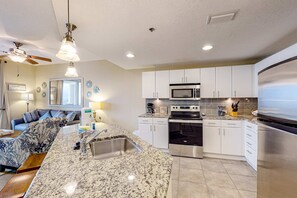 A modern kitchen with white cabinets, stainless steel appliances, and a granite countertop. - Wonderful gulf-view condo with a pool, hot tub & ocean-view balcony (Panama City Beach)