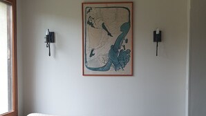 A room with a sofa, a wall-mounted painting, two wall sconces, a wooden ceiling beam, and a window. - Quiet 4-person vacation rental in the countryside, with amenities just a 5-minute walk away, a pool, and more (Maubec)