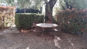 A round metal table with a metal bench, surrounded by a hedge and a large tree. - Quiet 4-person vacation rental in the countryside, with amenities just a 5-minute walk away, a pool, and more (Maubec)