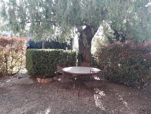 A round metal table with a metal bench, surrounded by a hedge and a large tree. - Quiet 4-person vacation rental in the countryside, with amenities just a 5-minute walk away, a pool, and more (Maubec)