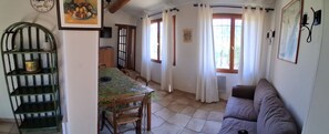 A dining area with a table covered in greenery, a wooden chair, and a green metal shelf with a yellow object on it. - Quiet 4-person vacation rental in the countryside, with amenities just a 5-minute walk away, a pool, and more (Maubec)