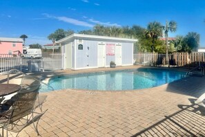 A swimming pool area with a covered changing room, a fenced patio, and a table with chairs. - Cozy coastal condo with shared pool and close to beach access (Panama City Beach)