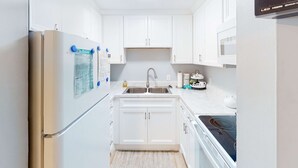 A compact kitchen with white cabinets, a stainless steel refrigerator, a double sink, and a microwave.