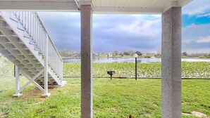 A covered outdoor area with a staircase leading to a higher level, a grassy area with a water body in the background, and a clear sky.