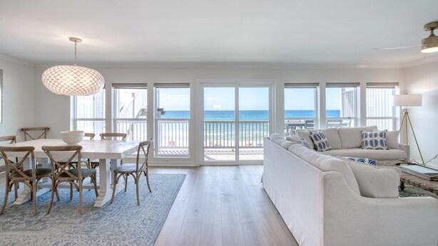 A spacious living room with a large white sofa, a dining table with chairs, and a view of the ocean through large sliding doors. - Gorgeous Gulf-front condo - step onto the beach from your private balcony (Santa Rosa Beach)