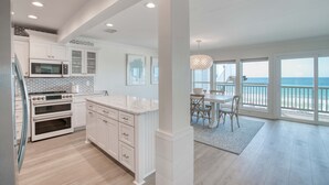A modern kitchen with white cabinetry, a large island, and a view of the ocean through the dining area. - Gorgeous Gulf-front condo - step onto the beach from your private balcony (Santa Rosa Beach)