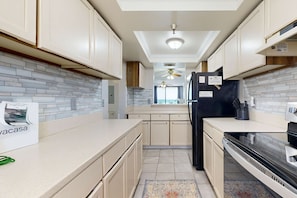A modern kitchen with light-colored cabinets, a black refrigerator, and a tiled backsplash. - Beachfront condo with Gulf views, pool, & private balcony - near Navarre Pier (Navarre Beach)