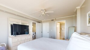 A bedroom with a large bed, a ceiling fan, a dresser, a TV, and a door leading to a bathroom. - Beachfront condo with Gulf views, pool, & private balcony - near Navarre Pier (Navarre Beach)