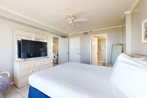 Une chambre à coucher avec un grand lit, un ventilateur de plafond, une commode, une télévision et une porte donnant sur une salle de bain.