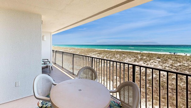 A balcony with a table and chairs, overlooking a beach with sand dunes and the ocean. - Beachfront condo with Gulf views, pool, & private balcony - near Navarre Pier (Navarre Beach)