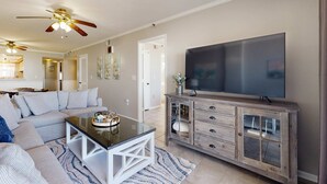 A living room with a sofa, coffee table, TV, and a wooden cabinet. - Beachfront condo with Gulf views, pool, & private balcony - near Navarre Pier (Navarre Beach)