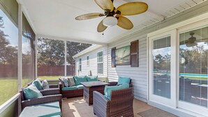 Une terrasse couverte, dotée de meubles en osier, d’un ventilateur de plafond et de grandes fenêtres.