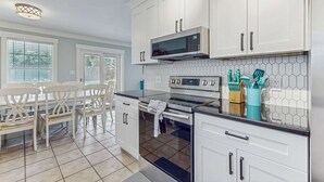 Une cuisine moderne avec des meubles blancs, un four à micro-ondes, un four traditionnel et un coin repas comprenant une table et des chaises.
