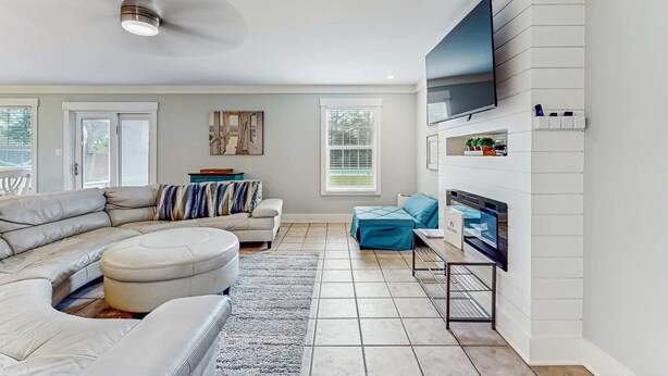 Un salon moderne avec un canapé d’angle, un pouf et un téléviseur à écran plat fixé au mur.