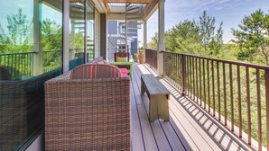Une terrasse en bois, agrémentée de meubles en osier et d’un banc, qui offre une vue sur un quartier résidentiel avec des arbres et des bâtiments modernes.