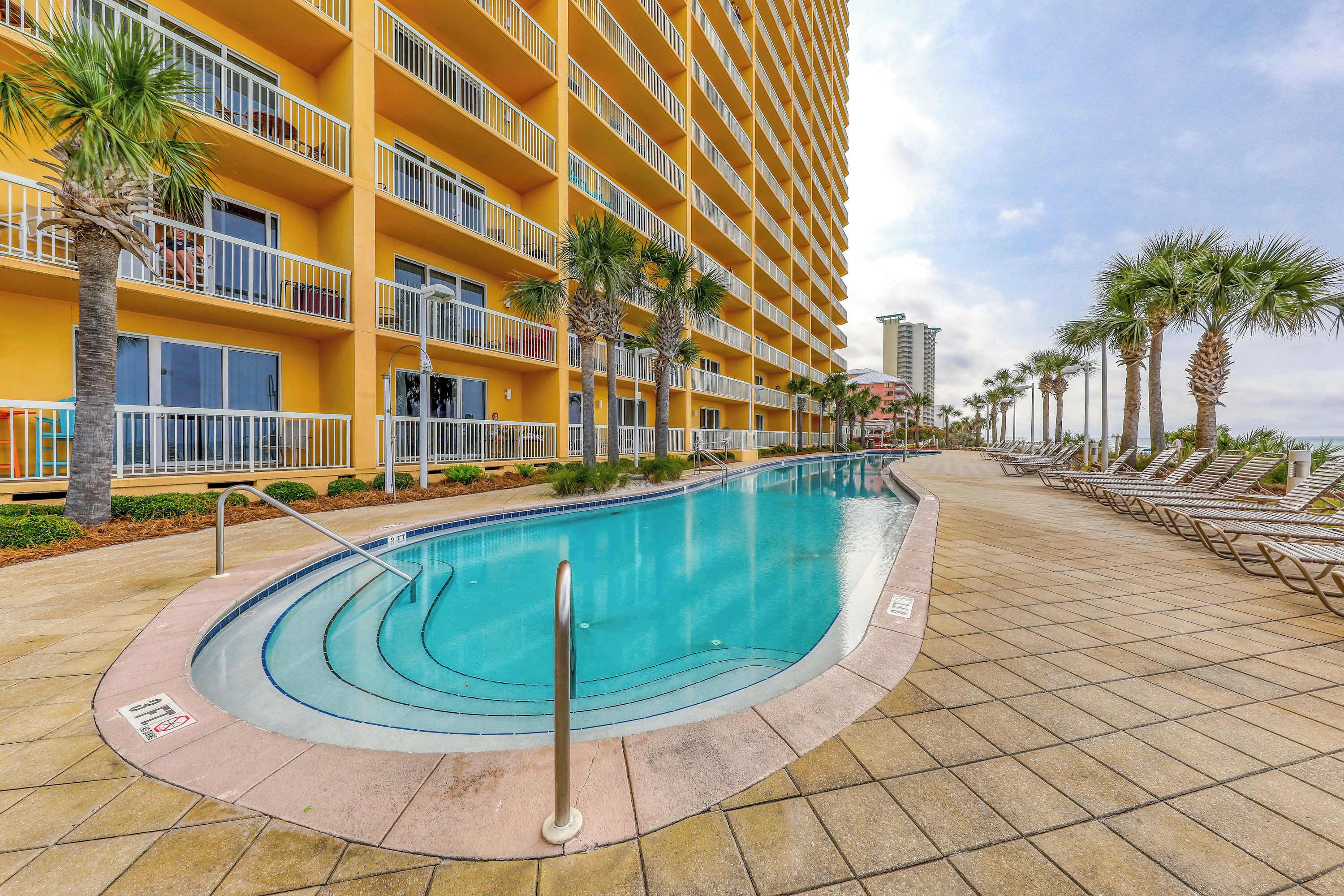 A hotel with a pool, palm trees, and a tiled walkway.