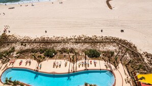 Oversigtsbillede af et strandresort med swimmingpool, strandstole og parasoller.