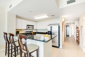 A modern kitchen with white cabinets, stainless steel appliances, and a central island with bar stools. - High-rise condo with pool & ocean views - walk to the beach (Panama City Beach)