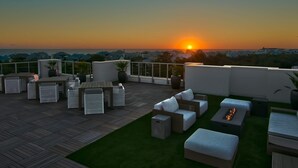 A rooftop terrace with outdoor furniture, a fire pit, and a view of the sunset over the ocean. - Modern condo with pool, hot tub, gym, wrap-around balcony, & AC (Inlet Beach)