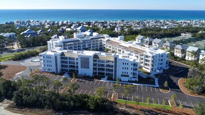A modern hotel with multiple floors, a central courtyard, and a view of the ocean. - Modern condo with pool, hot tub, gym, wrap-around balcony, & AC (Inlet Beach)