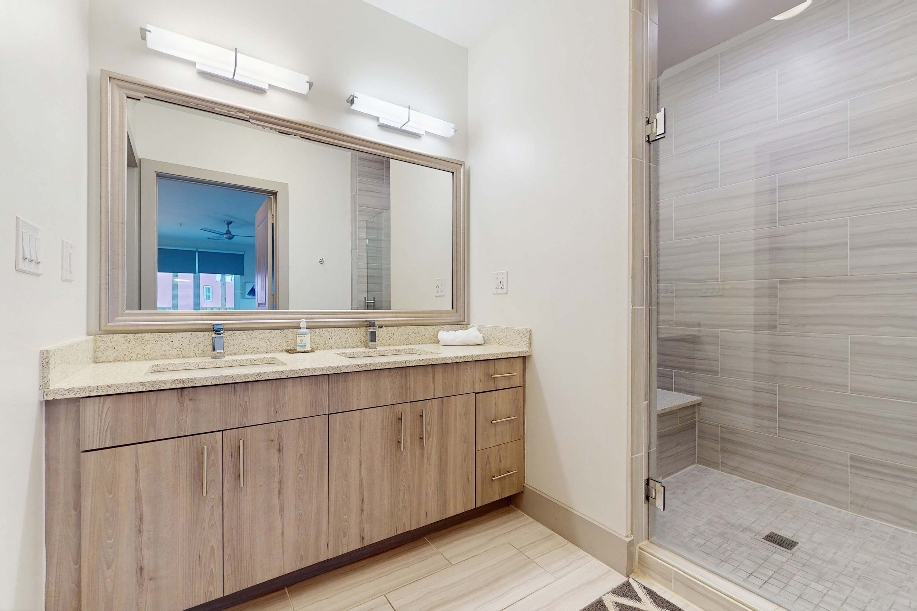 Un baño moderno con un espejo grande, tocador de madera y ducha a ras de suelo con paredes alicatadas.