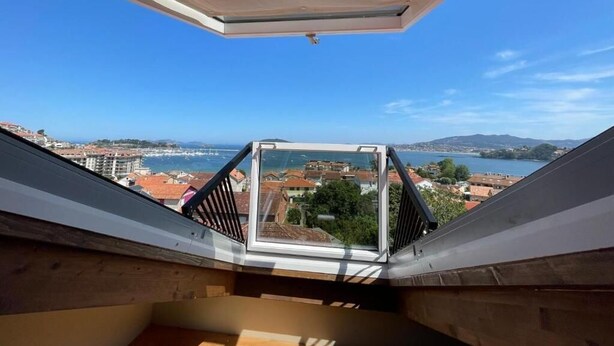 Vista desde un punto elevado, probablemente un balcón o terraza, sobre un pueblo costero con edificios y una extensión de agua.