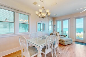 A dining area with a glass table, white chairs, and a chandelier. There are large windows with blinds and a view of the ocean. - Gulf-front home with breathtaking views in gated Carillon Beach community (Panama City Beach)