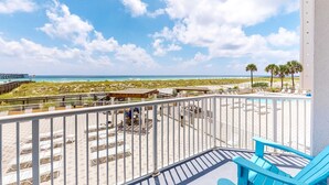 A balcony with a view of the beach, lounge chairs, and a distant bridge. - First-Floor Gulf Front Condo with Shared Pool & Hot Tub (Navarre Beach)