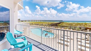 A balcony with turquoise chairs, a pool, and a view of the beach and ocean. - First-Floor Gulf Front Condo with Shared Pool & Hot Tub (Navarre Beach)