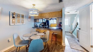 Una cucina moderna con isola centrale, pavimento in legno e zona pranzo con tavolo rotondo e sedie blu.