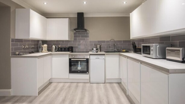 A modern kitchen with white cabinets, grey tiled backsplash, stainless steel appliances, and a central island. - Charming 2-bedroom Apartment in Central Kingston Upon Thames (Kingston Upon Thames)