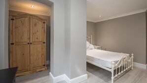 A bedroom with a bed, a wooden wardrobe, and a white nightstand. - Charming 2-bedroom Apartment in Central Kingston Upon Thames (Kingston Upon Thames)