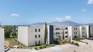 Un edificio moderno con parcheggio, aree verdi e montagne sullo sfondo.