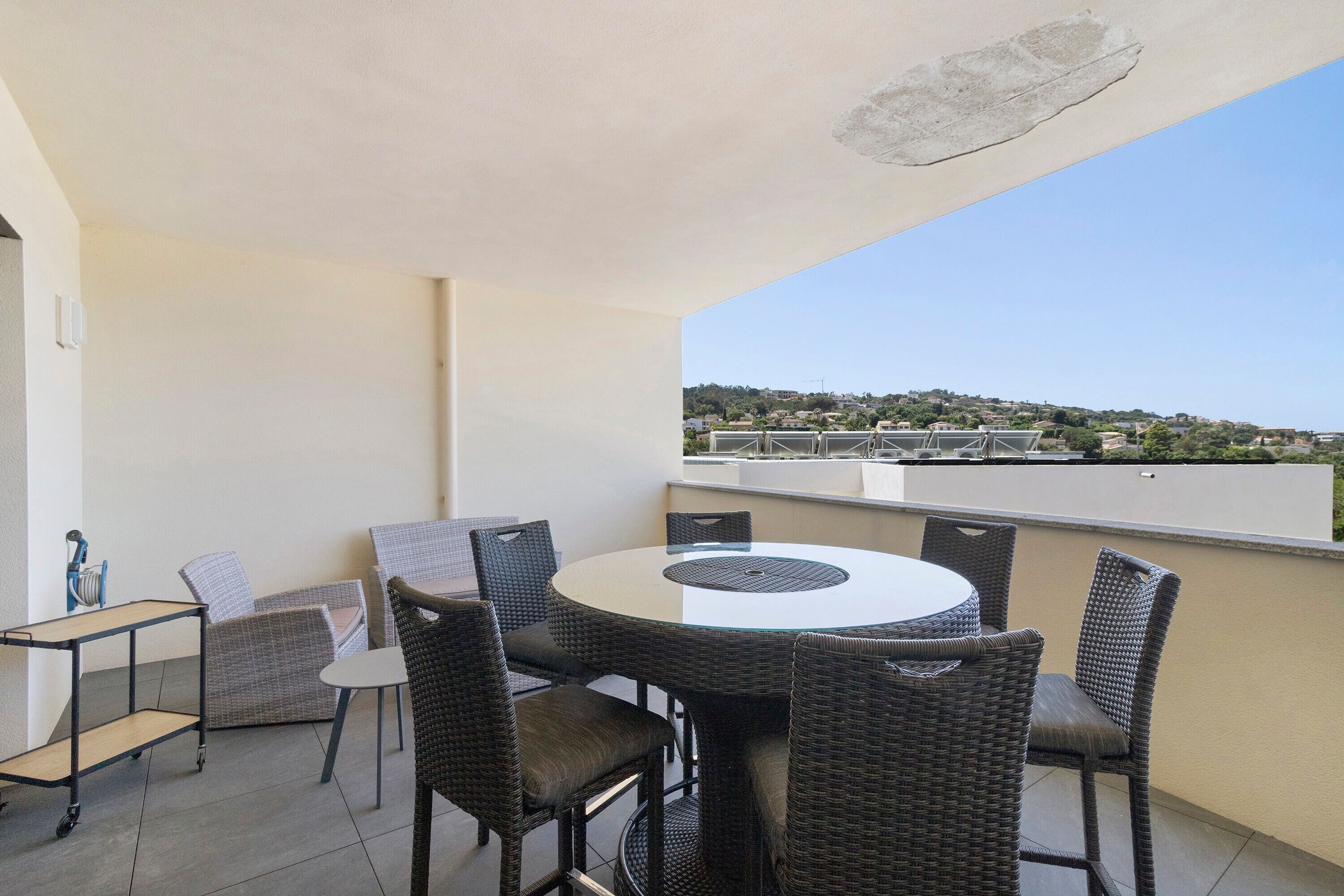 Ein Balkon mit rundem Tisch und Korbstühlen, mit Blick auf ein Wohngebiet.