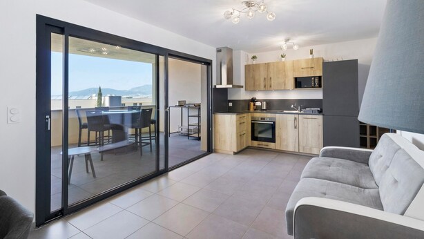 Una cucina moderna con zona pranzo, divano e vista attraverso una porta vetrata.