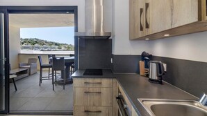 Una cucina moderna con cappa in acciaio inossidabile, mobili in legno, lavello integrato e zona pranzo con posti a sedere all'aperto.