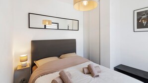 Un letto rifatto con testiera, una lampada da comodino, uno specchio e un quadro appeso al muro.