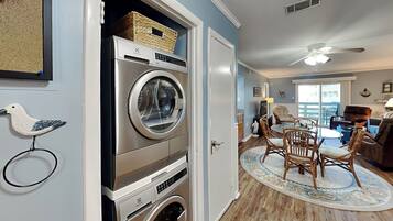 A laundry room with stacked washers and dryers, a dining area with a round table and chairs, and a ceiling fan.
