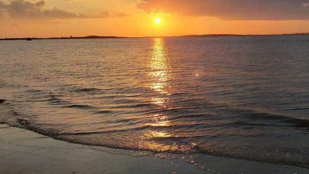 A sunset over a calm sea with a boat in the distance. - Lighthouse Point 31B | Excellent Views, Pool Access (Tybee Island)