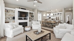 Una sala moderna con mobiliario blanco, una chimenea y un comedor con una cocina al fondo.